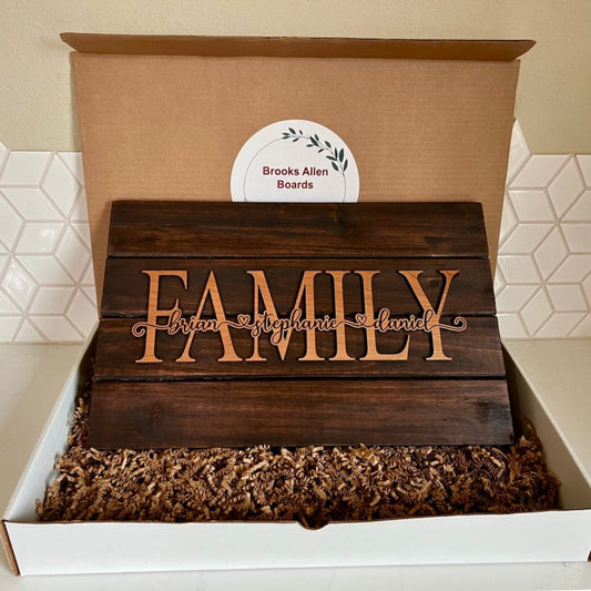 3D Pallet-Style sign with  'FAMILY' on top, 'Brian Stephanie Daniel' engraved across the word family, in a box, in a box, brand 'Brooks Allen Boards' logo visible on box lid.